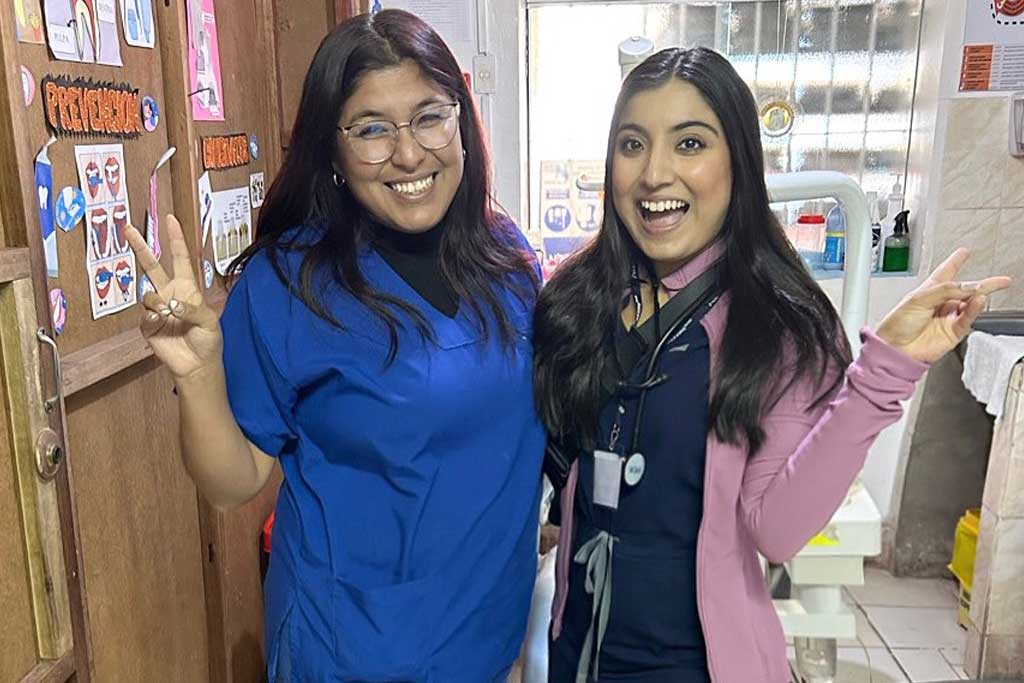 Two women in scrubs smiling and making peace signs in a clinic