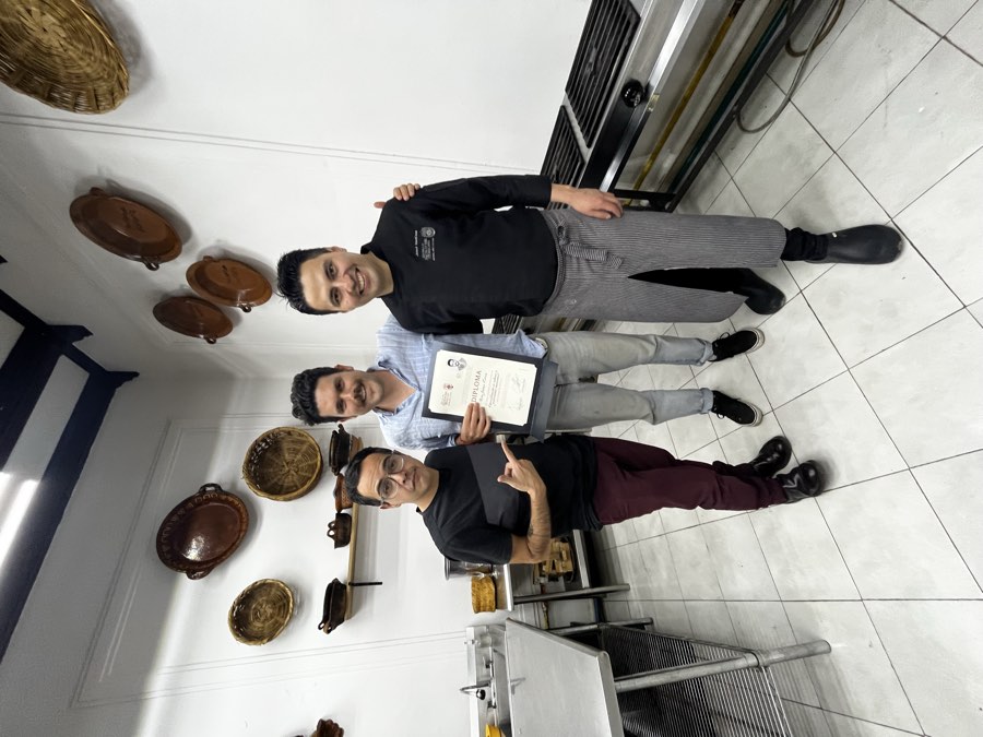 A student holding a cooking class diploma, standing between two chefs in a kitchen